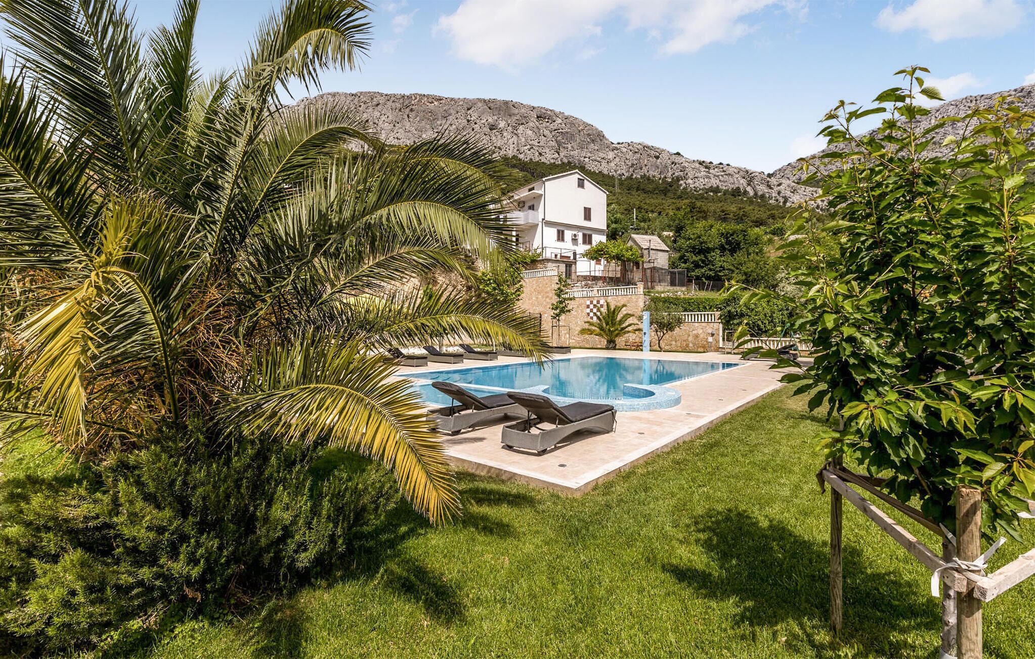 Una piscina con sillas de descanso, un edificio blanco de varios pisos y un paisaje montañoso de fondo.