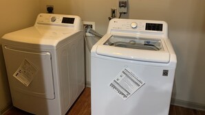 Uma área de lavanderia com duas máquinas de lavar LG brancas, uma de abertura frontal e outra superior, com painel de controle e entrada de água.