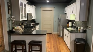 Uma cozinha moderna com piso de madeira, armários brancos e uma ilha central com banquetas.