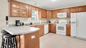 A kitchen with wooden cabinets, a white refrigerator, a stove, a microwave, and a coffee maker.