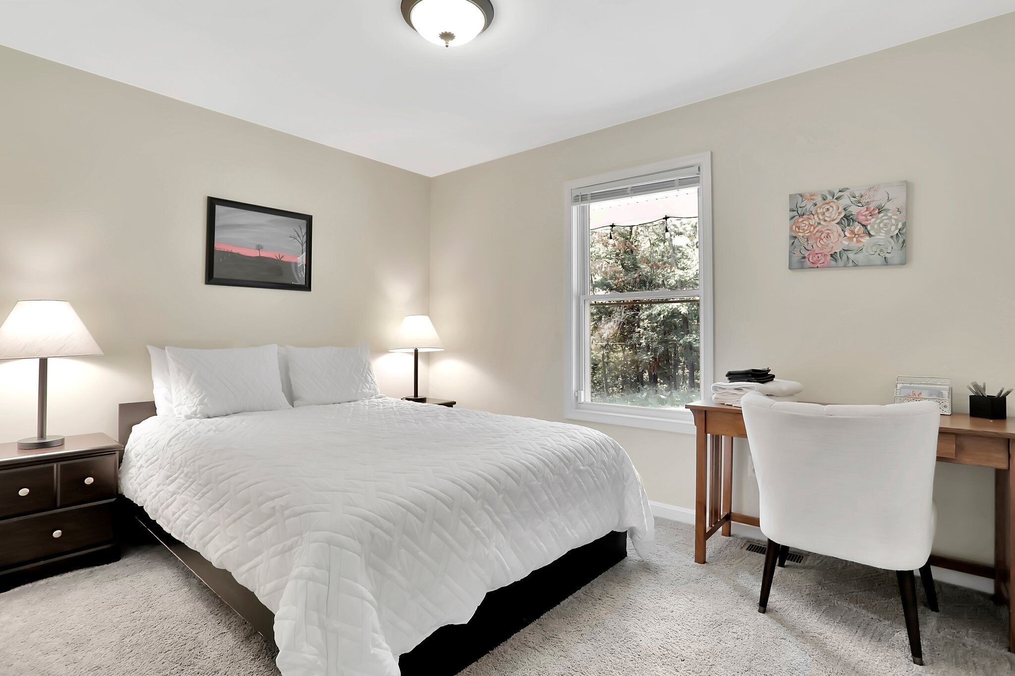 A bedroom with a bed, bedside lamps, a desk, and a chair.
