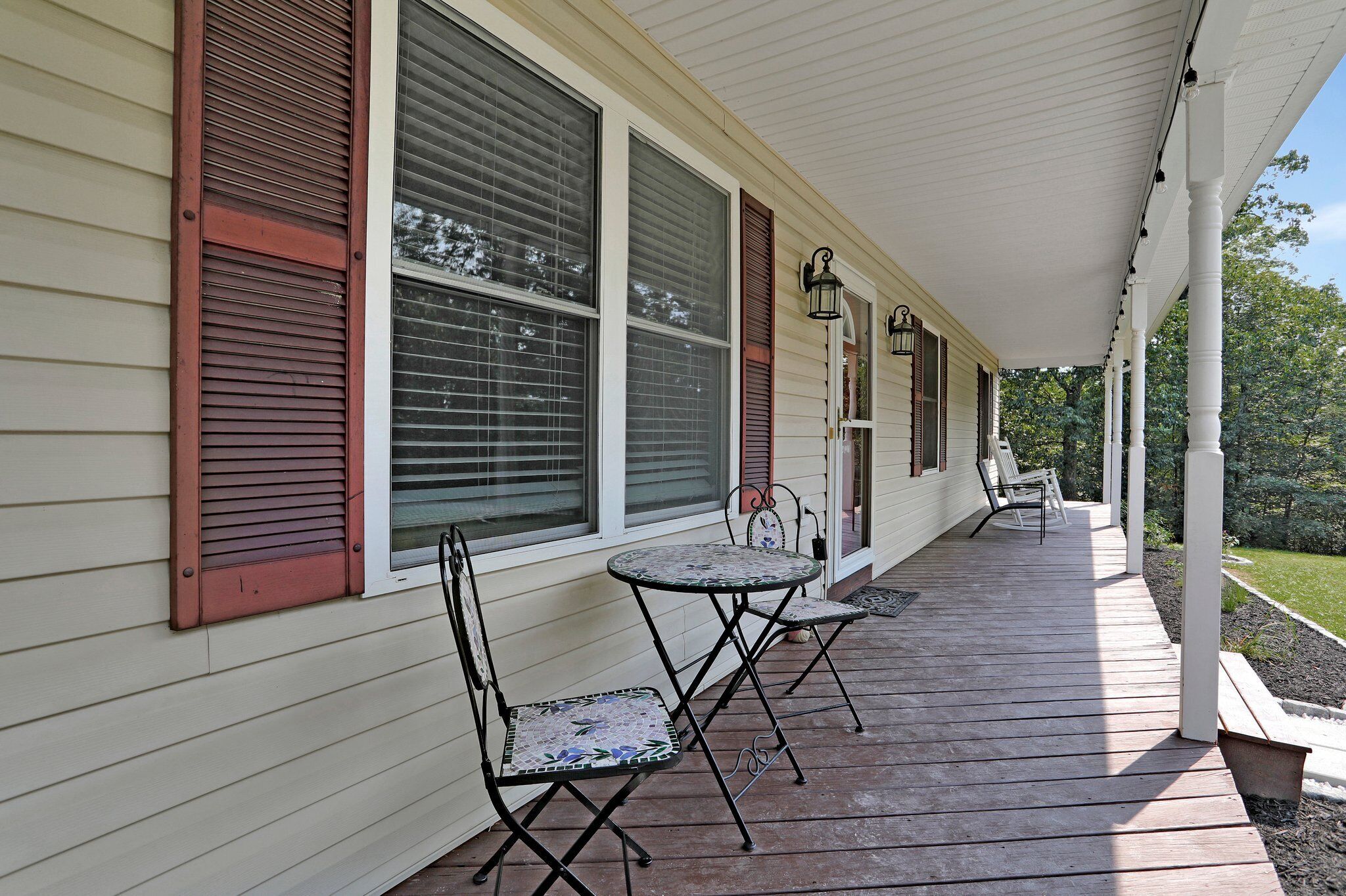 A covered porch with a table and chairs, large windows with shutters, and a white railing.