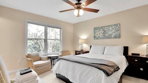 A bedroom with a bed, a chair, a desk, a ceiling fan, and a window.