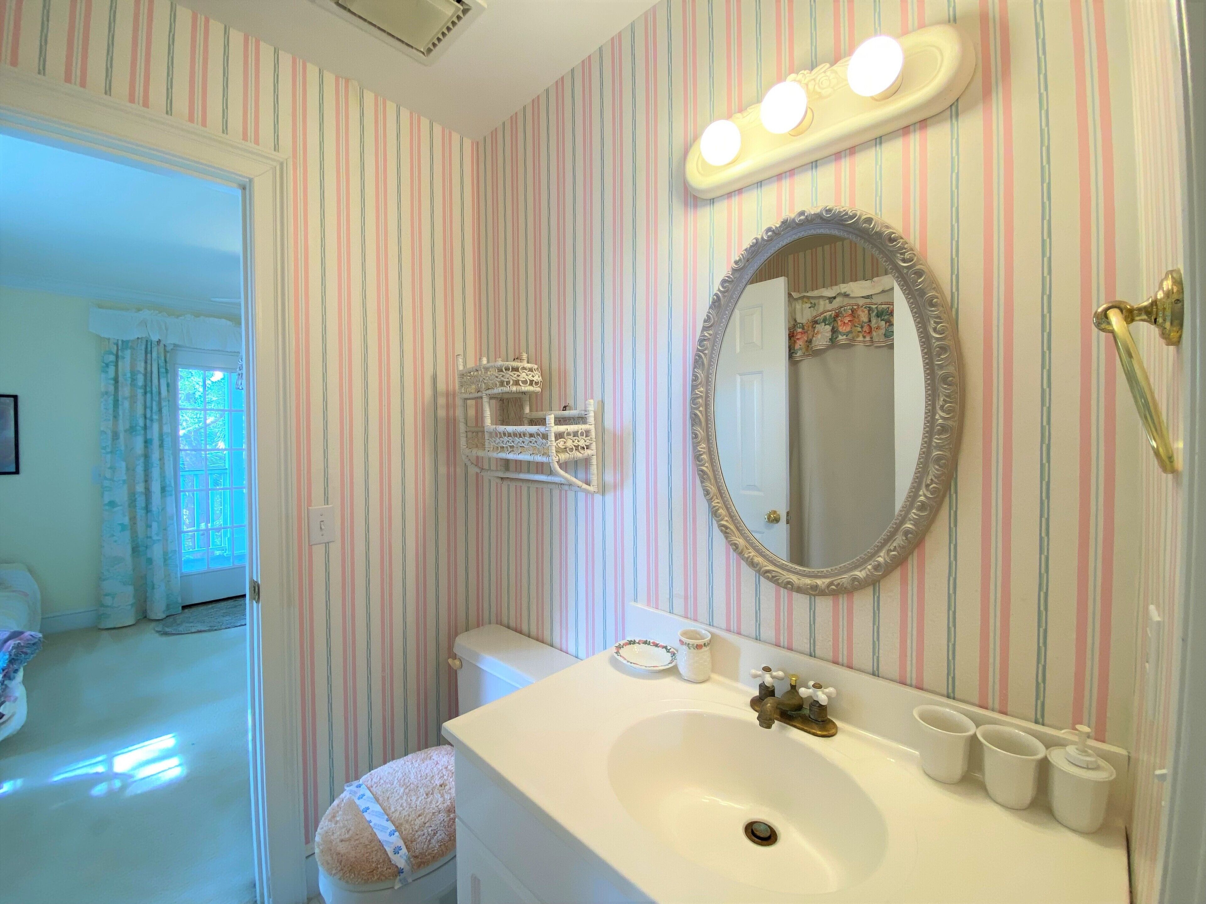 A bathroom with a striped wallpaper, a white sink with a mirror, and a toilet with a floral seat cover.
