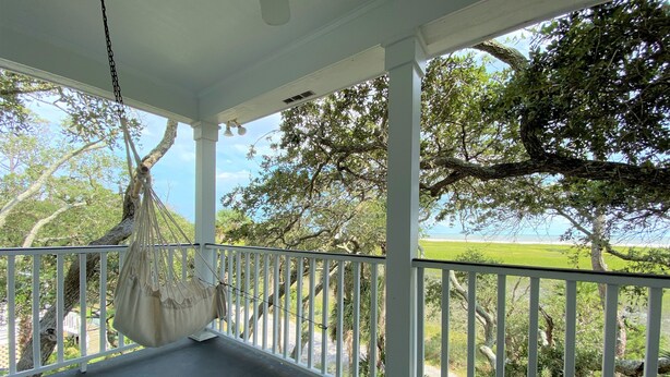 A covered porch with a hanging hammock, white railings, and a view of a green landscape and trees. - Marsa's Place-Marsh/Creek/Ocean Views; Easy Beach Access;Dogs Welcome (Edisto Island)