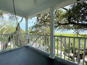 A covered porch with a hanging hammock, white railings, and a view of a green landscape and trees. - Marsa's Place-Marsh/Creek/Ocean Views; Easy Beach Access;Dogs Welcome (Edisto Island)