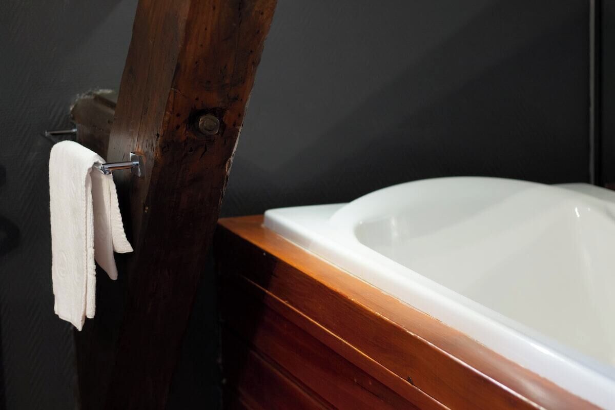 Une baignoire dotée d’un cadre en bois et une serviette suspendue à un crochet en métal.