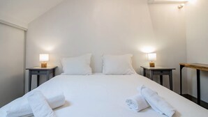 Un lit bien fait, avec du linge de lit blanc et deux oreillers, de part et d’autre duquel se trouvent des tables de chevet avec des lampes.