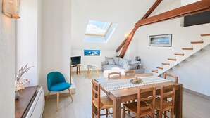 Un appartement moderne de style « loft », comprenant un coin repas, un canapé, un téléviseur et un escalier avec des poutres en bois apparentes.