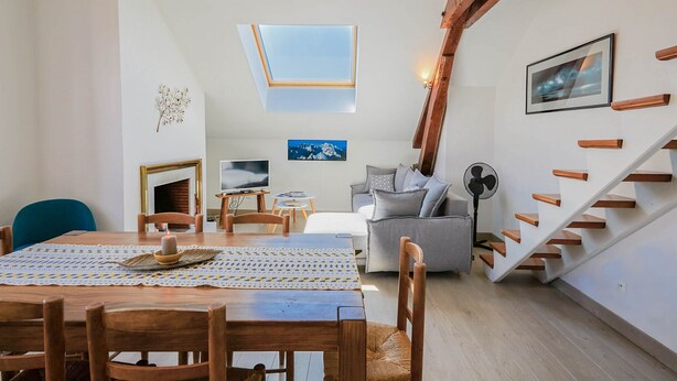 Un salon chaleureux avec un escalier en bois, un coin repas avec une table et des chaises, et une fenêtre au plafond.