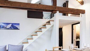 Un intérieur moderne avec un escalier en bois, un coin repas avec une table dressée pour deux personnes et un tableau encadré au mur.
