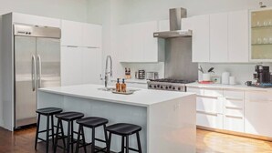 Une cuisine moderne dotée d’un îlot central, de tabourets de bar, d’un réfrigérateur en acier inoxydable et d’une cuisinière.