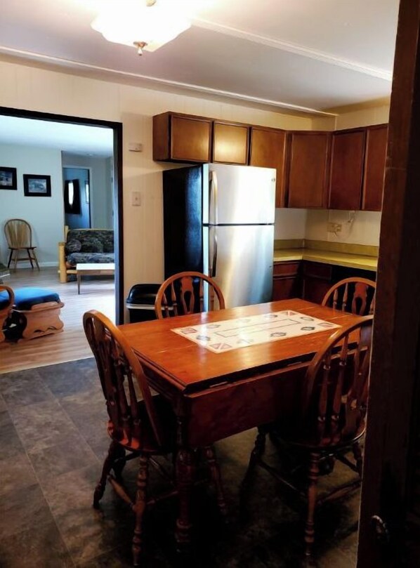 Une cuisine de taille réduite, dotée de meubles de rangement en bois, d’un réfrigérateur et d’une table à manger avec des chaises.