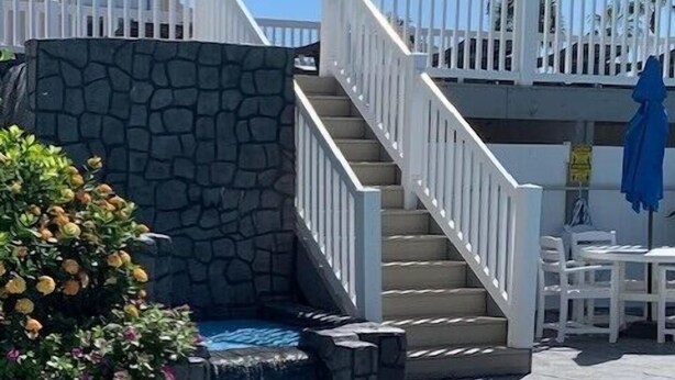 Zona de piscina con pared de piedra, escaleras y sillas de descanso.