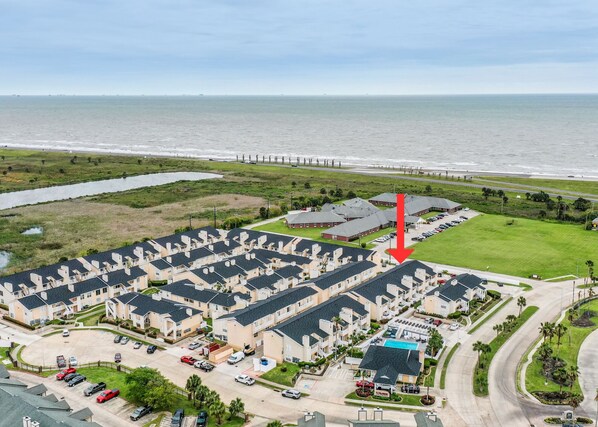 Uma área residencial costeira com uma fileira de casas geminadas, um estacionamento e uma praia ao fundo.