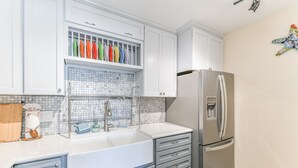 Una cocina moderna con armarios blancos, un refrigerador de acero inoxidable, salpicadero de azulejos y una encimera con diversos utensilios de cocina.