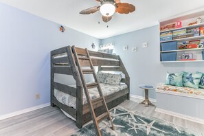 Uma cama beliche com escada, um ventilador de teto, uma estante e uma pequena mesa redonda.
