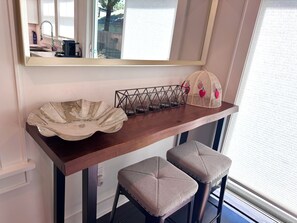 Un comptoir de cuisine agrémenté d’un saladier décoratif, d’un panier en fil métallique et d’un autre panier orné de motifs de fruits. Deux tabourets sont placés sous le comptoir.