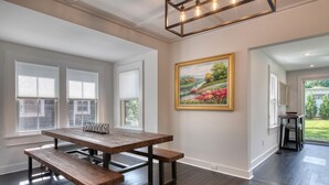 Una habitación amplia con una mesa de madera y bancos, ventanas grandes con persianas y un cuadro en la pared.