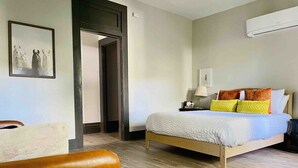 Un dormitorio con cama, una silla, una puerta y un equipo de aire acondicionado.