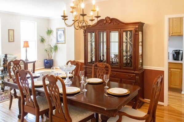 Une salle à manger avec une table en bois dressée pour six personnes, entourée de chaises assorties. Un grand buffet en bois, doté de portes en verre, est placé derrière la table.