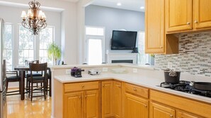 Une cuisine moderne avec des meubles en bois, un plan de travail blanc, une cuisinière à gaz et un téléviseur à écran plat placé au-dessus du plan de travail.