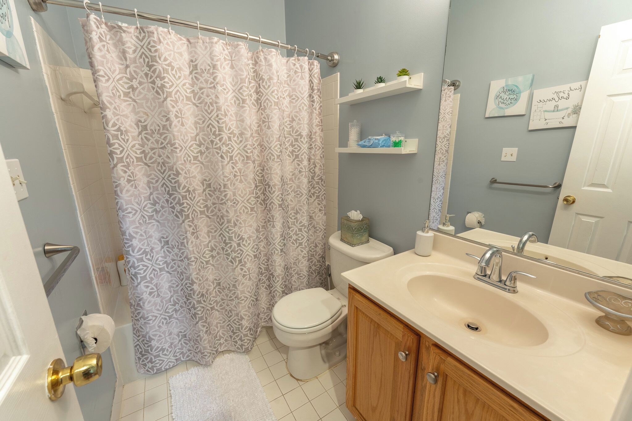 A bathroom with a shower curtain, toilet, sink, and wooden cabinets.