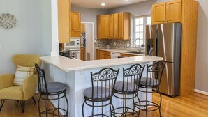 Une cuisine moderne avec des meubles en bois, un réfrigérateur en acier inoxydable et un coin bar doté de tabourets en métal.