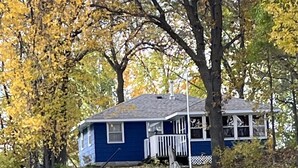 Uma casa com um cais que se estende sobre a água, cercada por árvores com folhas amarelas.