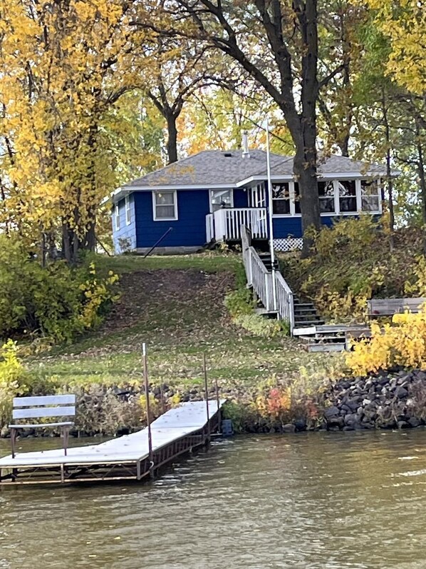 A house with a dock extending into a body of water, surrounded by trees with yellow leaves.