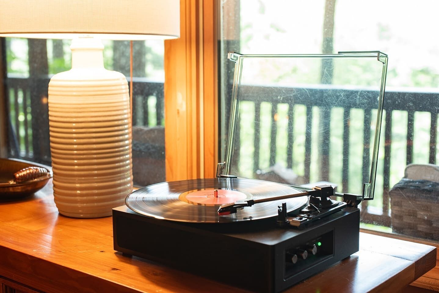 A turntable on a wooden table with a lamp and a window view.