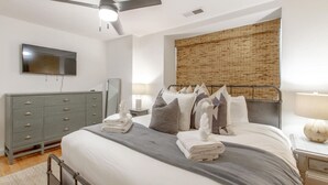 Un dormitorio con cama, ventilador de techo, televisor, cómoda y ventana con persiana de bambú.