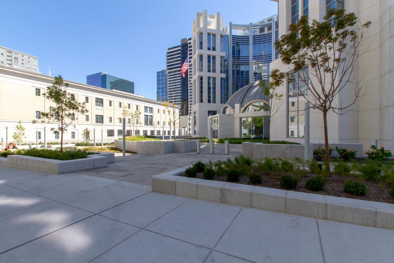 A modern urban plaza with a mix of architectural styles, including a curved glass building and a white building with a flag.