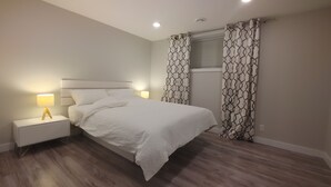 A bedroom with a bed, nightstands, and patterned curtains. - Beautiful two bedroom + den lower level suit (Calgary)