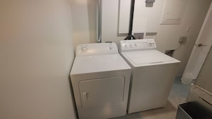 A compact laundry room with a front-loading washer and dryer, a mirror, and a door with a handle. - Beautiful two bedroom + den lower level suit (Calgary)