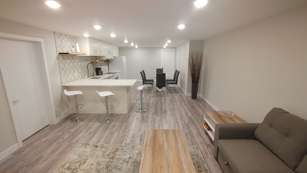 A modern kitchen with a central island, bar stools, and a dining area with a table and chairs. - Beautiful two bedroom + den lower level suit (Calgary)