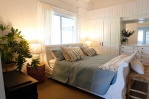 Ein Schlafzimmer mit einem Bett, Nachttischlampen, einem Schminktisch, einem Spiegel und einer Topfpflanze.