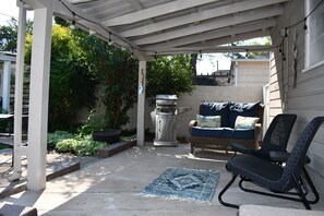 Ein überdachter Patio-Bereich mit einem Korbsessel, einem Schaukelstuhl und einem dekorativen Teppich.
