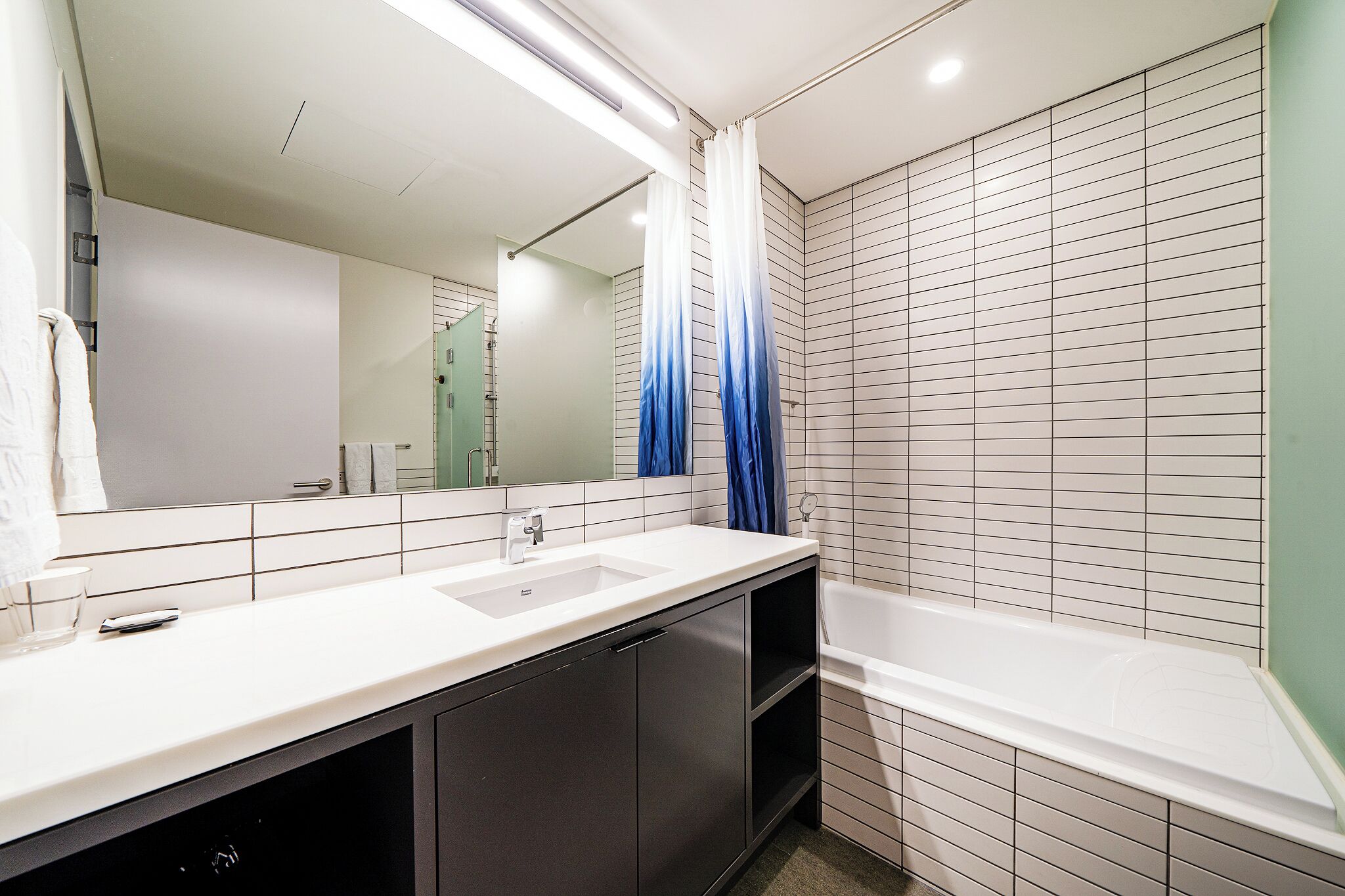 Een moderne badkamer met een witte wastafel, donkere kastjes, een grote spiegel en een witte badkuip.