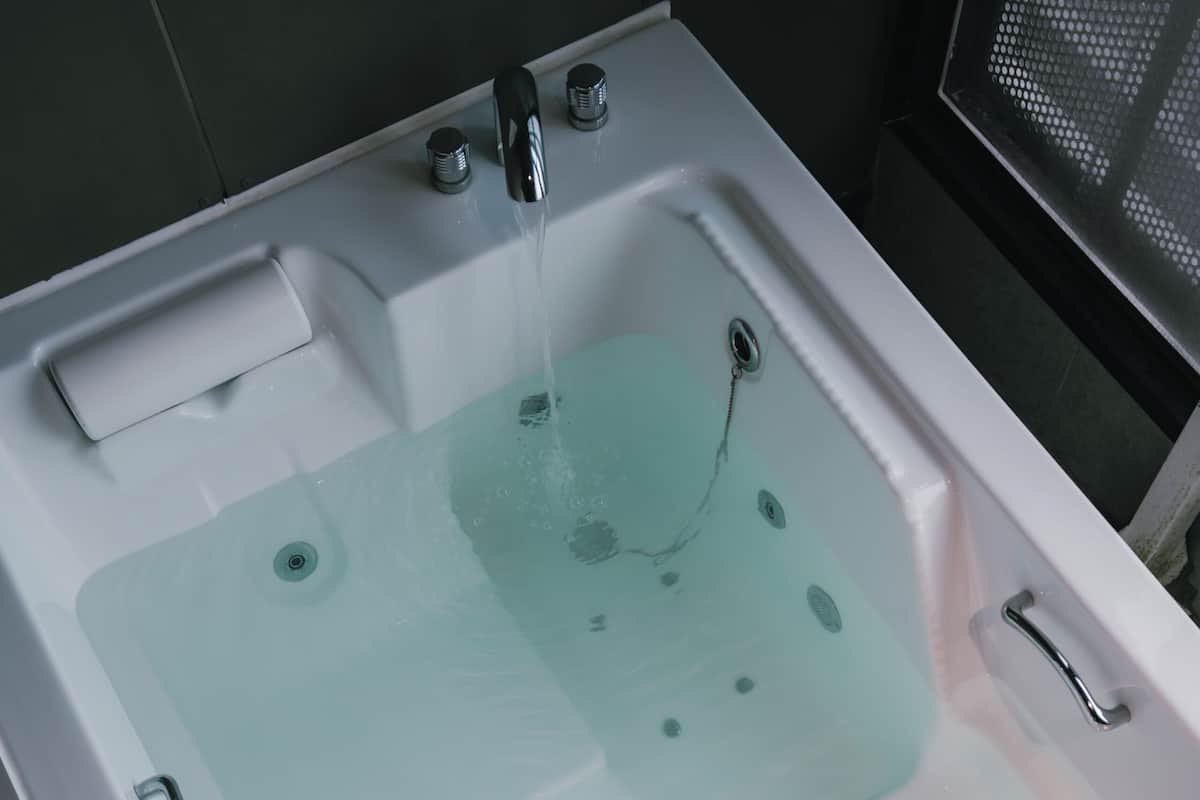 A white bathtub with a glass panel, a faucet, and a control panel.