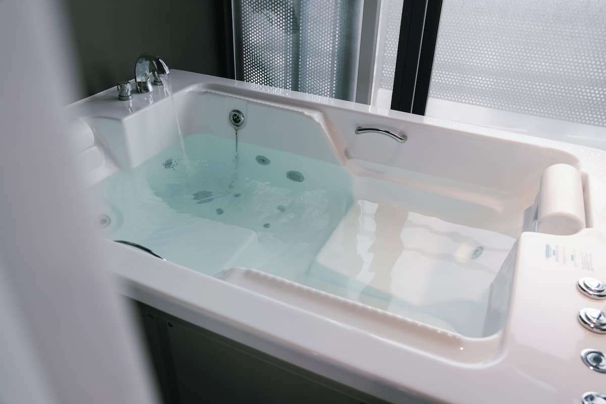 A bathtub with a glass panel, a faucet, and a control panel.