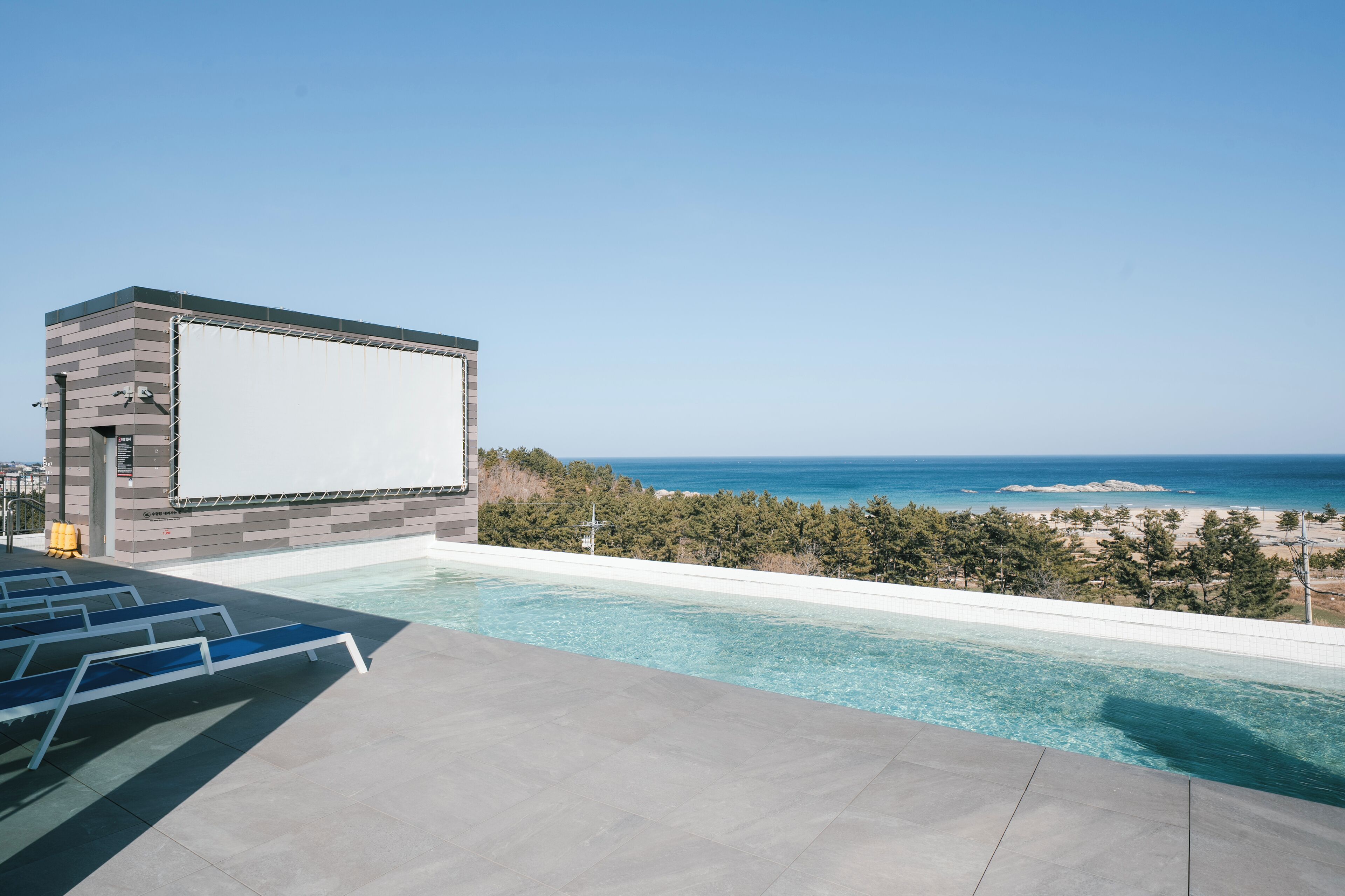 A rooftop pool with clear blue water, a beach view, and a modern building with a large screen.