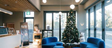 Un hall d’entrée moderne, décoré d’un sapin de Noël, avec des sièges bleus et un comptoir d’accueil.