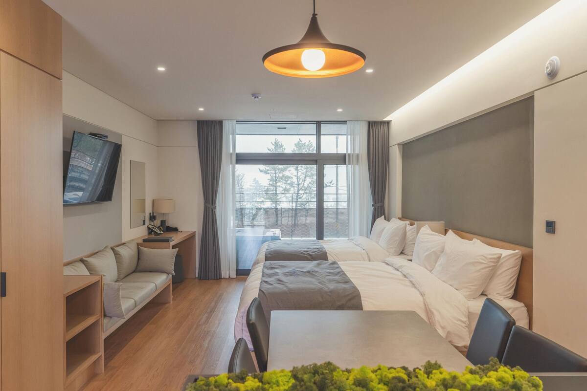 A modern hotel room with a large bed, a desk, a sofa, and a TV.