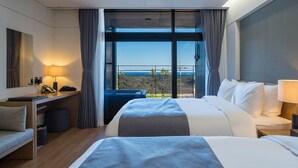 Una habitación de hotel moderna con dos camas, un escritorio, una silla, un ventanal con cortinas y vistas al exterior.