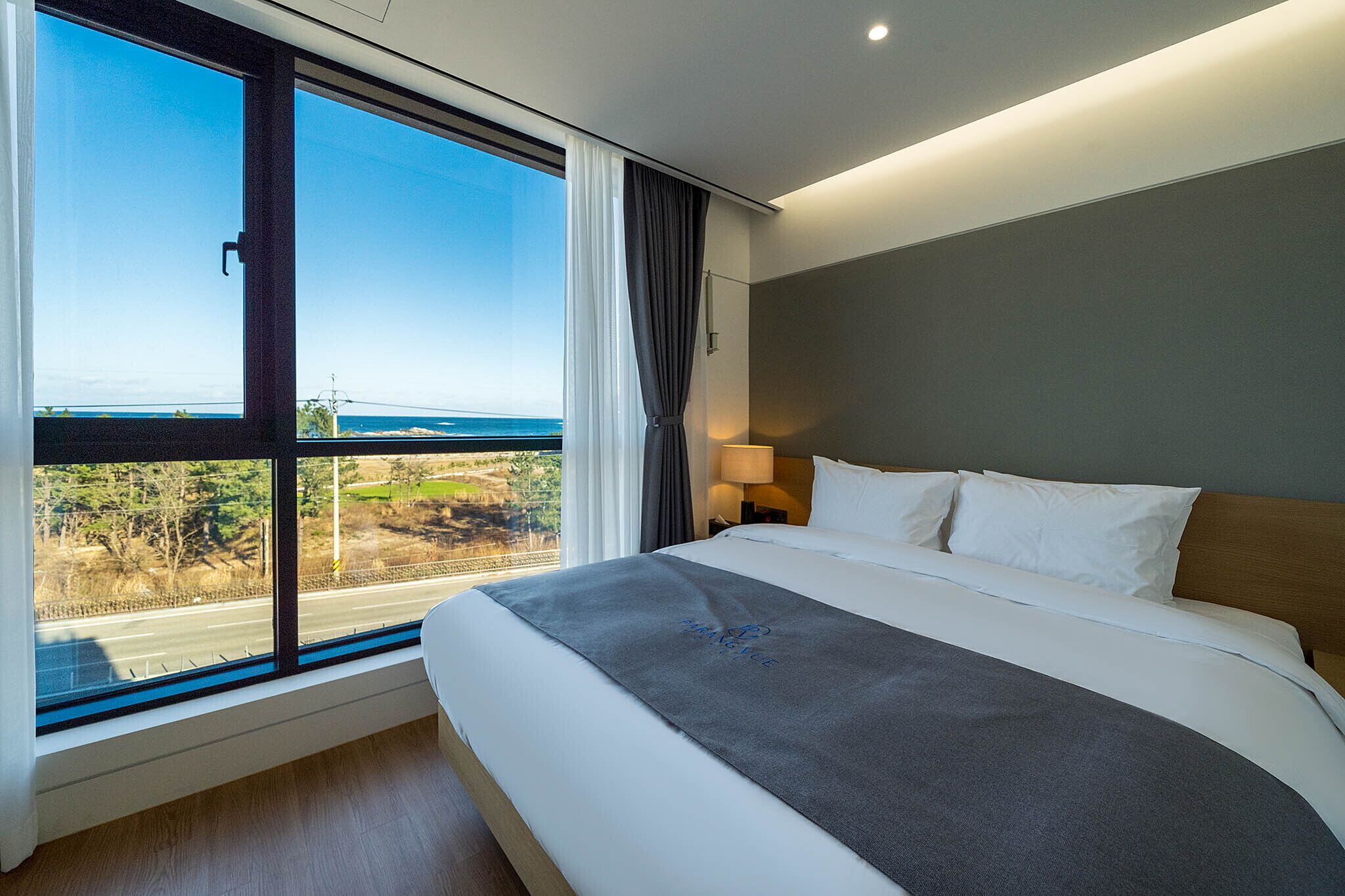 A hotel room with a large window offering a view of a road and greenery.