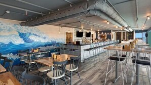 Un restaurante con un mural de olas, zona de bar y asientos modernos.