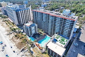 A high-rise hotel with multiple floors, a rooftop pool, and a beach area with umbrellas.
