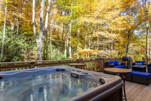 Un bain à remous sur une terrasse en bois, agrémentée de mobilier d’extérieur, avec une forêt en arrière-plan.