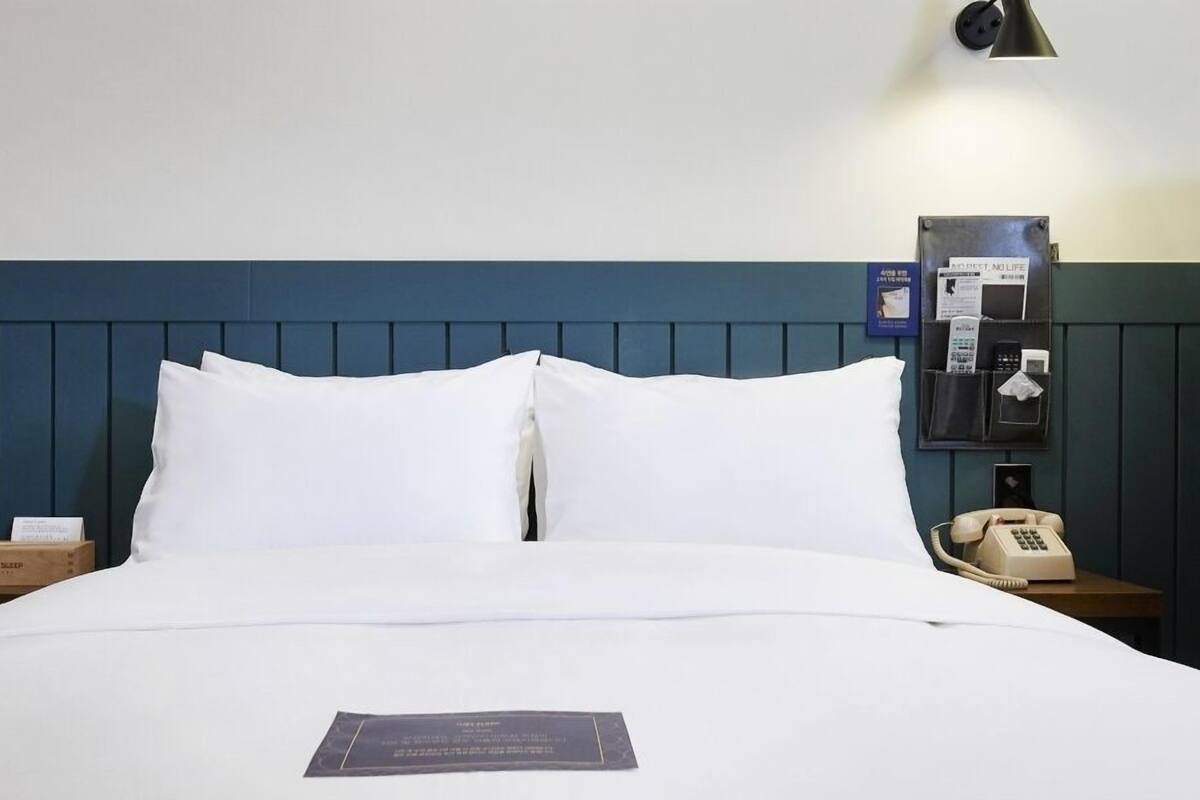 Una habitació d'hotel amb un llit ben fet, una taula de nit amb una làmpada, un telèfon i una estació de càrrega penjada a la paret.